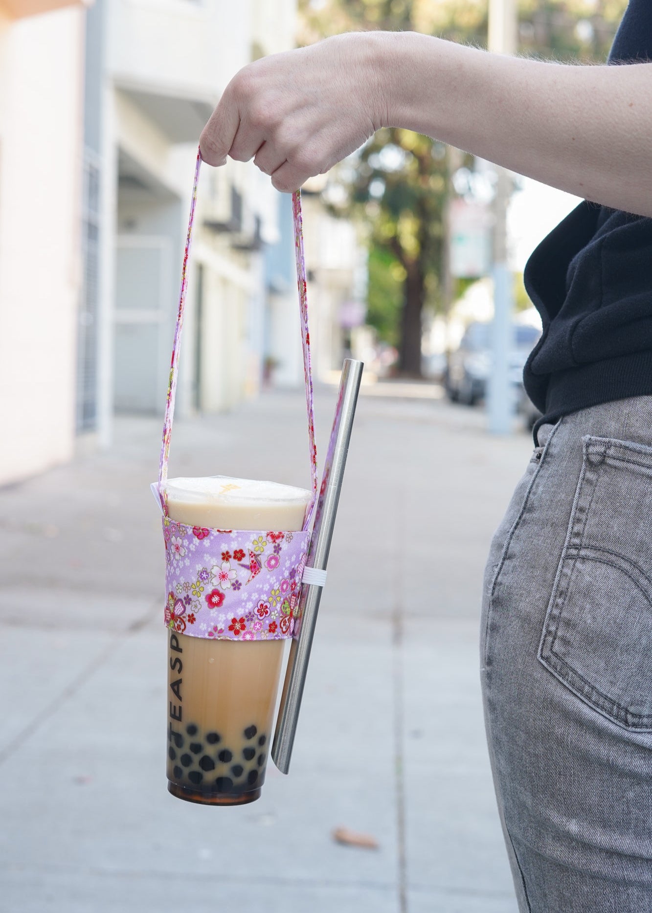 Person holding a floral-patterned cup with a straw on a sidewalk