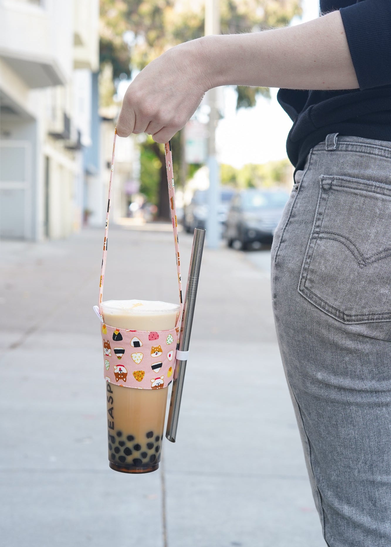 Person holding a bubble tea with a colorful sleeve and straw on a sidewalk.