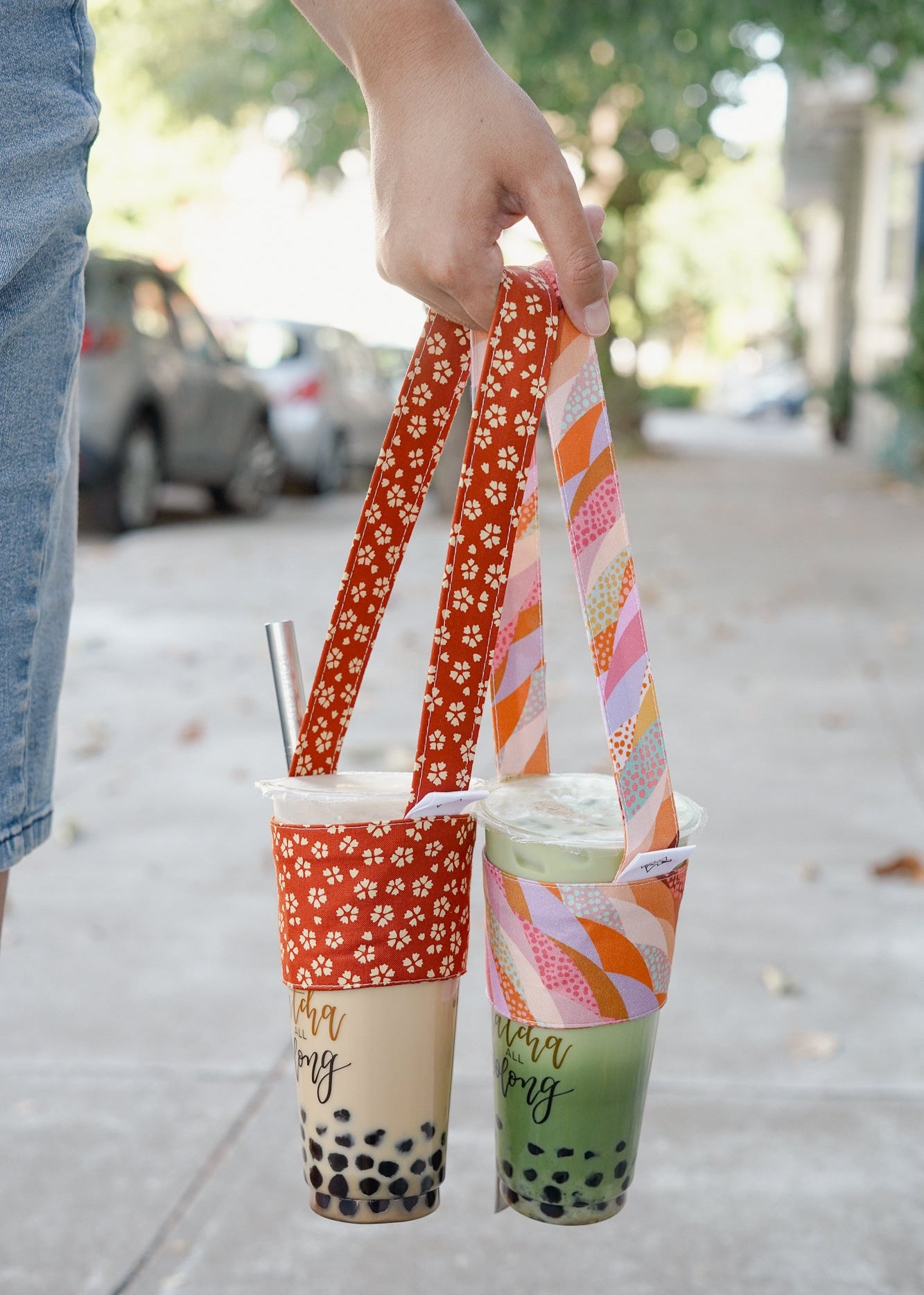 Two bubble tea cups with colorful straws held by a person on a sidewalk.