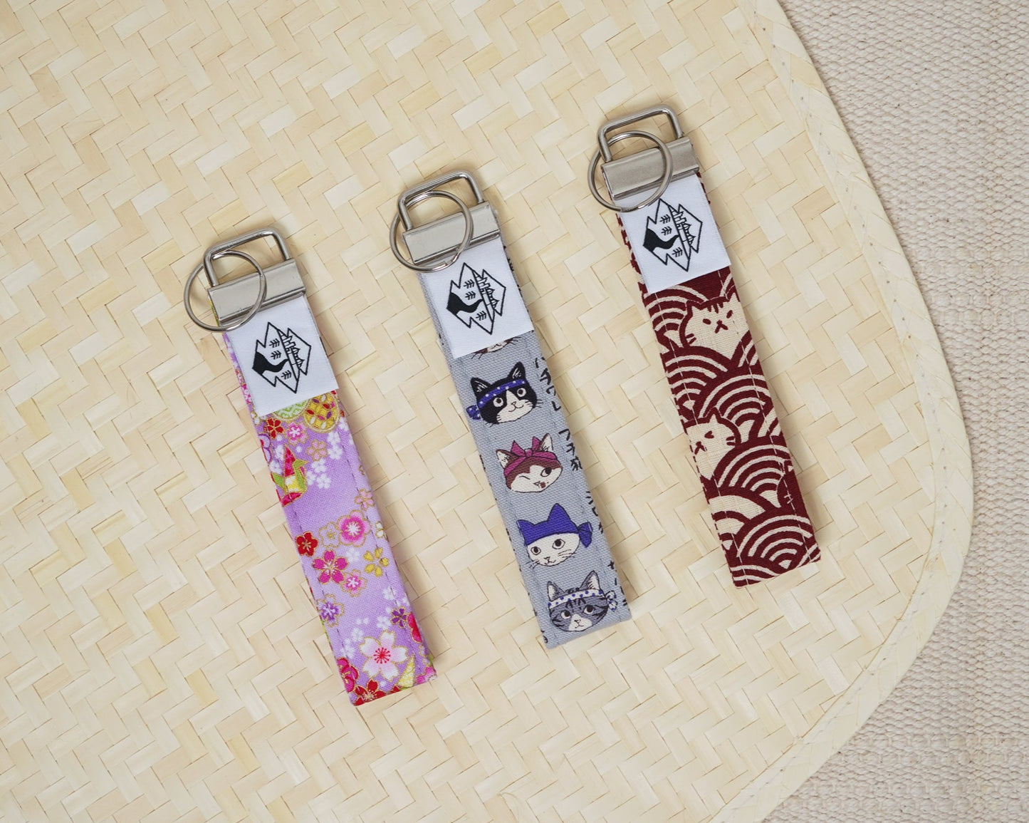 Three fabric keychains with cat designs on a textured surface