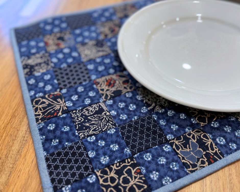Blue patchwork placemat made with Quilters Grid with a white plate on a wooden surface