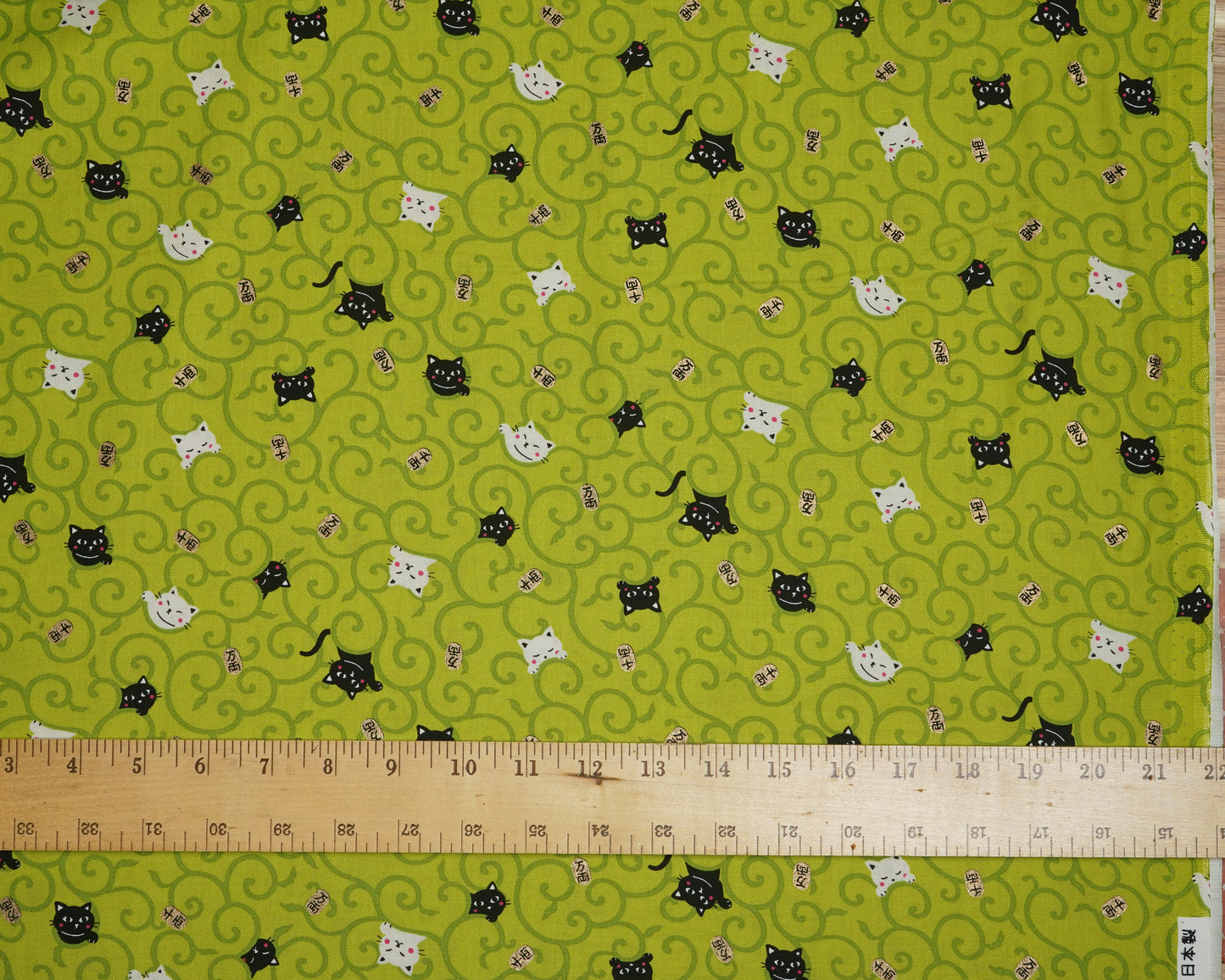 Fabric with cat pattern on a green background with a ruler at the bottom.