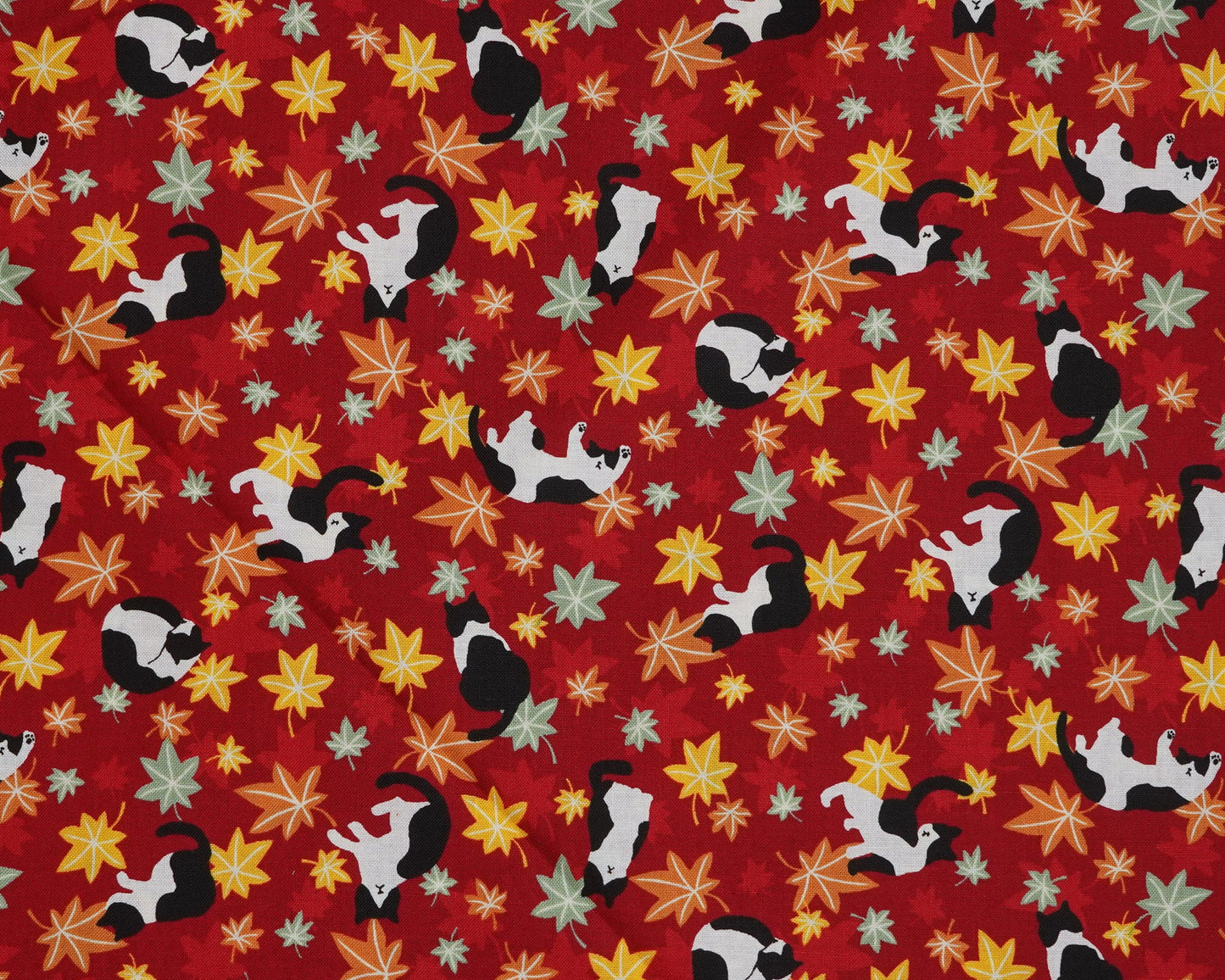 Pattern of small black and white cats on a red background with colorful leaves.