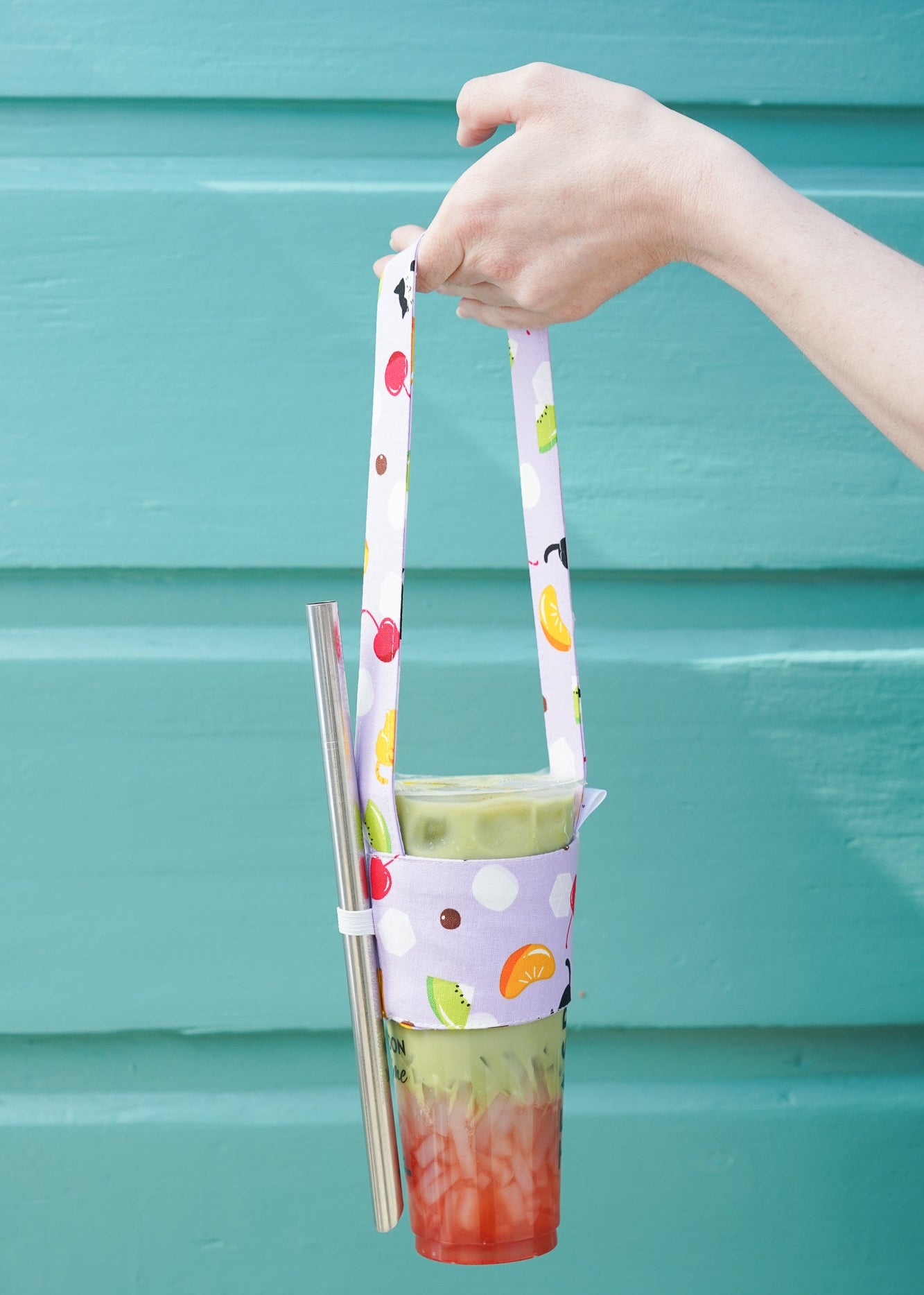 Hand holding a colorful drink holder with a glass against a teal background