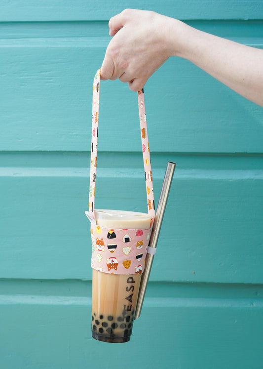 Hand holding a bubble tea cup with a colorful strap against a teal background