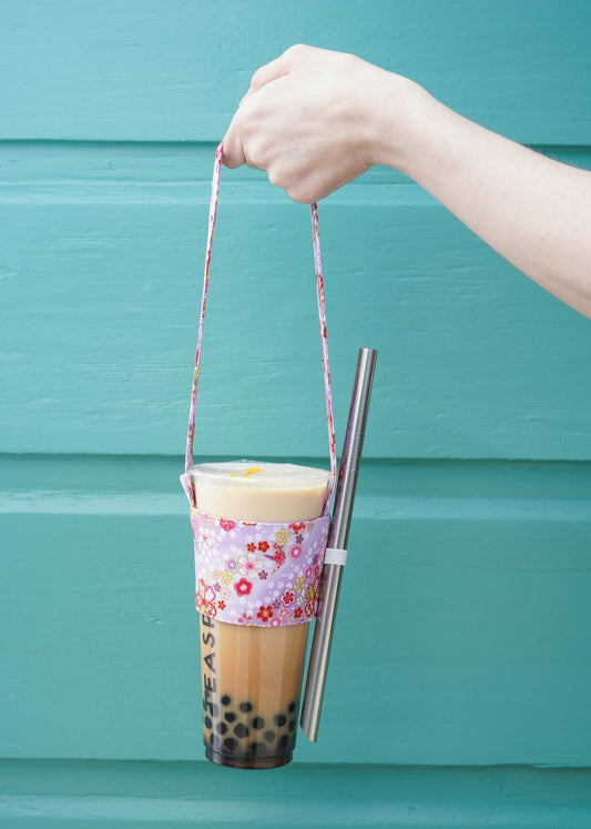 Hand holding a bubble tea with a colorful sleeve against a teal background