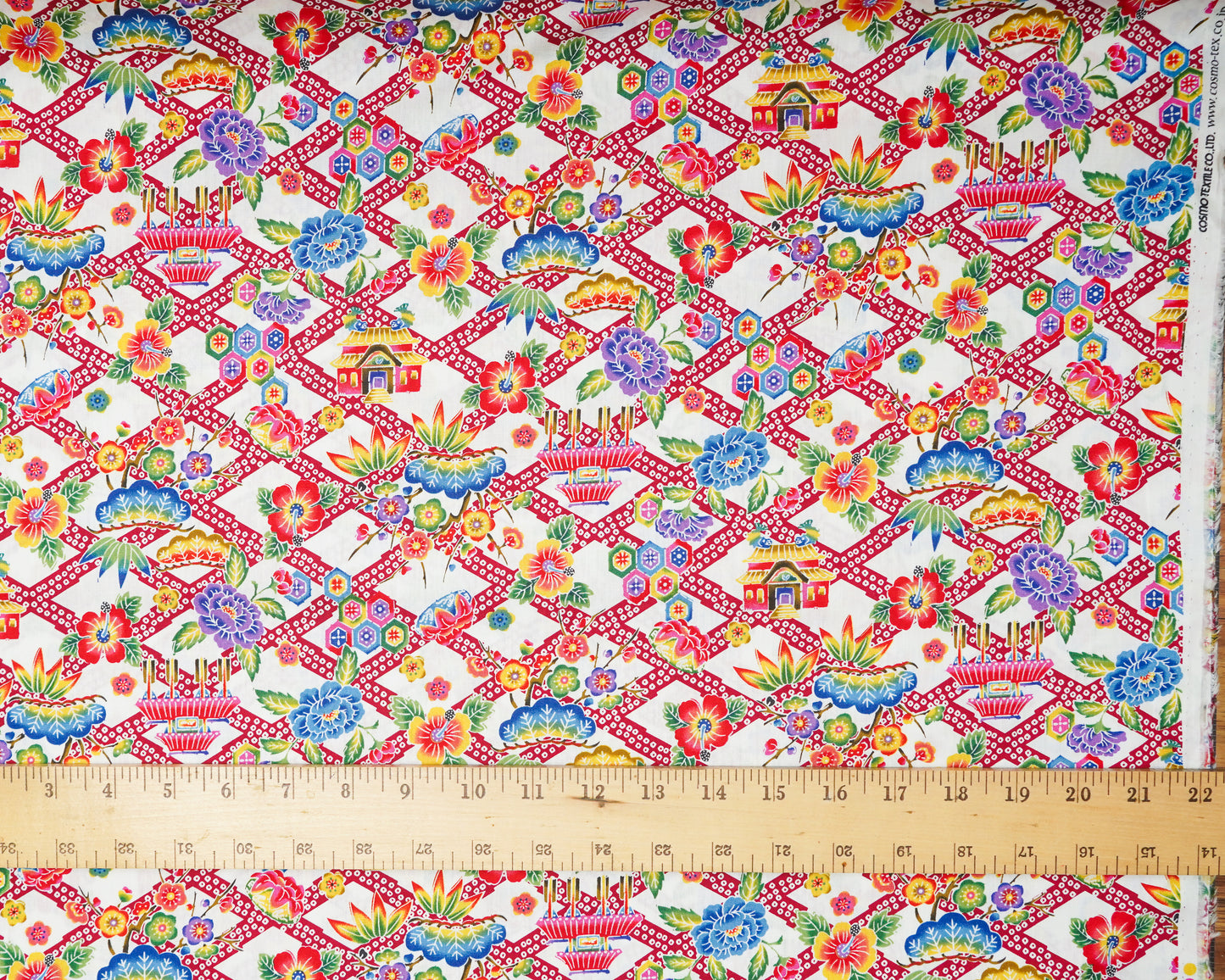 Colorful fabric pattern with geometric design and floral elements on a white background, measured with a ruler at the bottom.