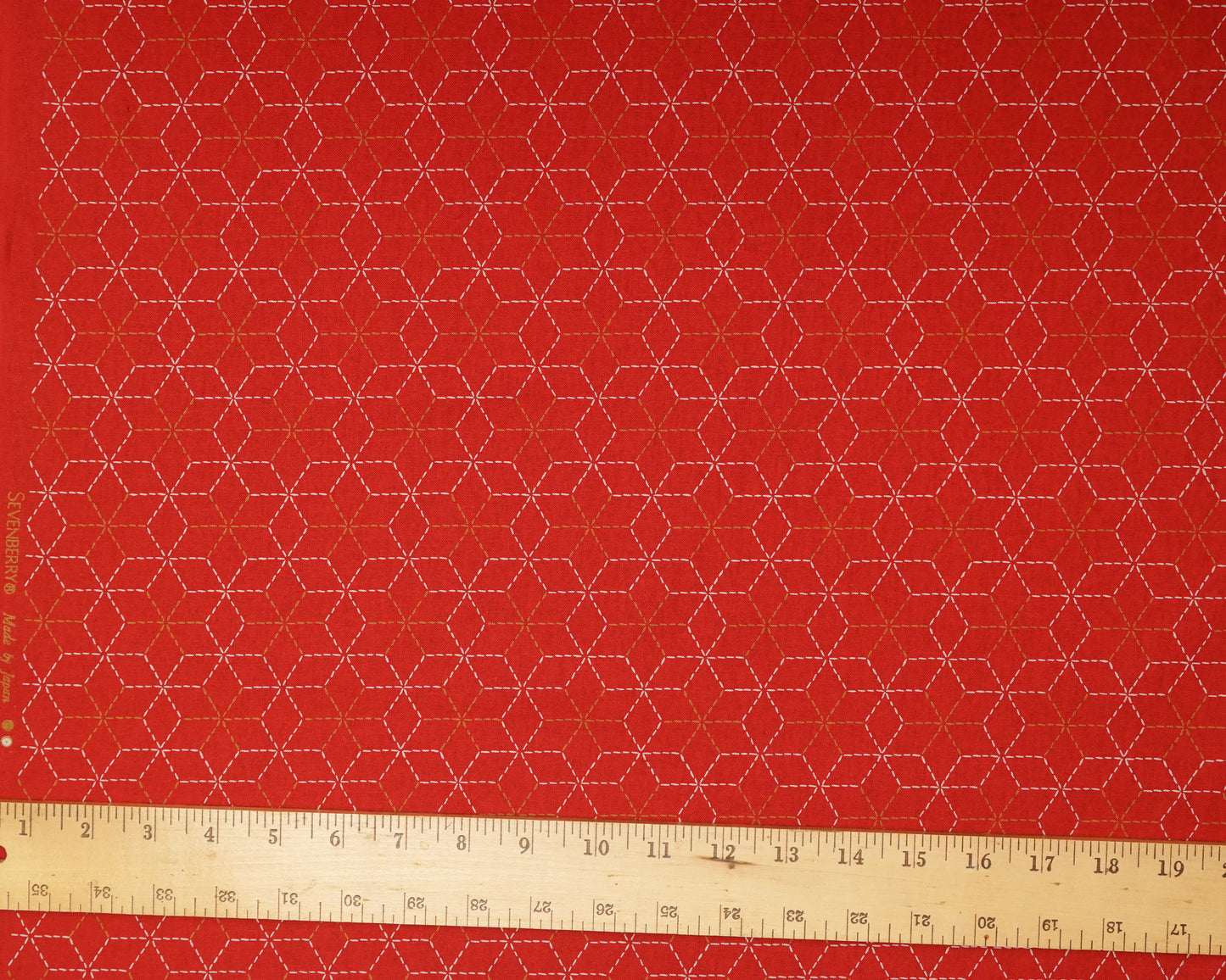 Red fabric with geometric pattern and a ruler at the bottom for scale.