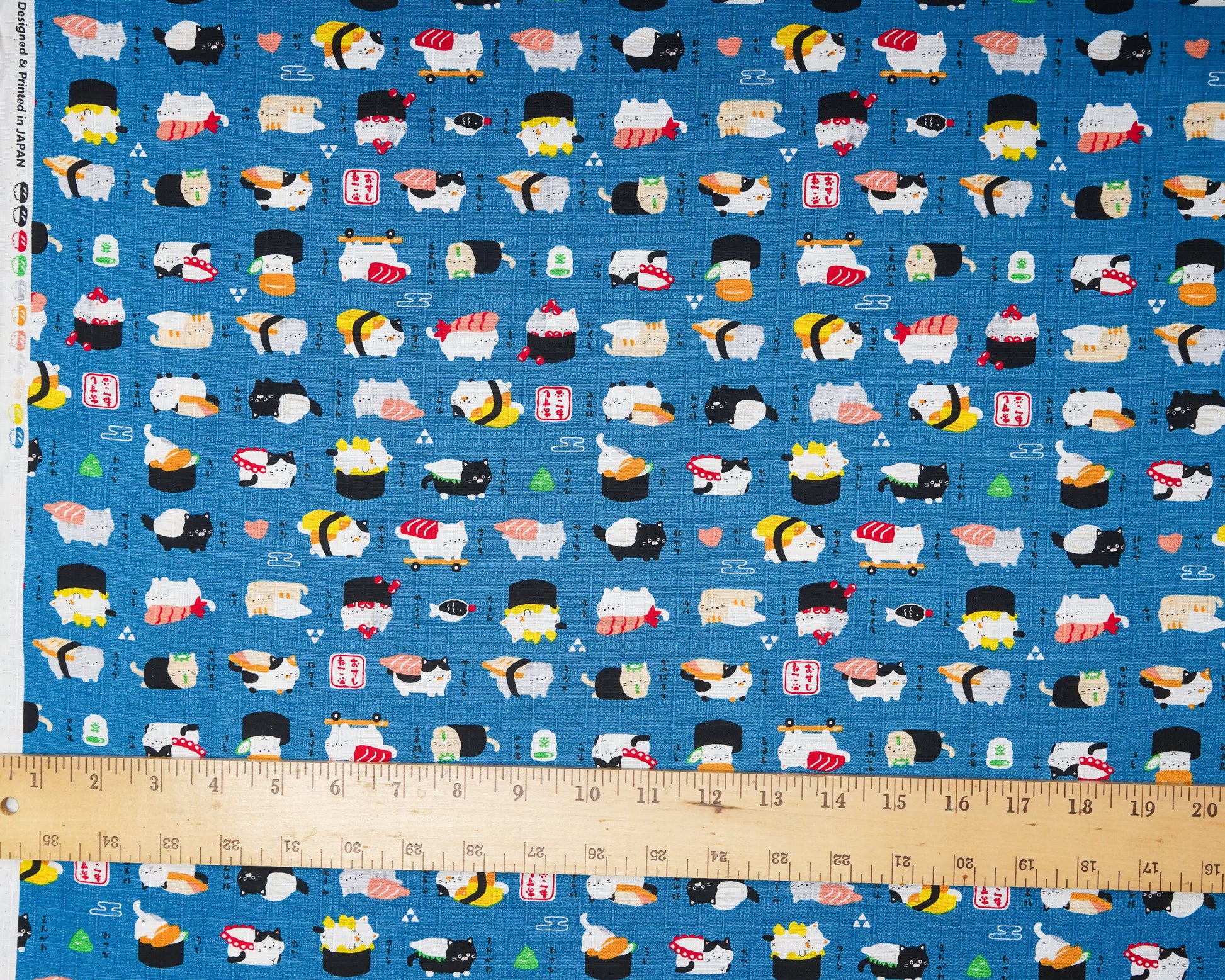 Fabric with cartoon sushi design on a blue background, ruler at the bottom for scale.