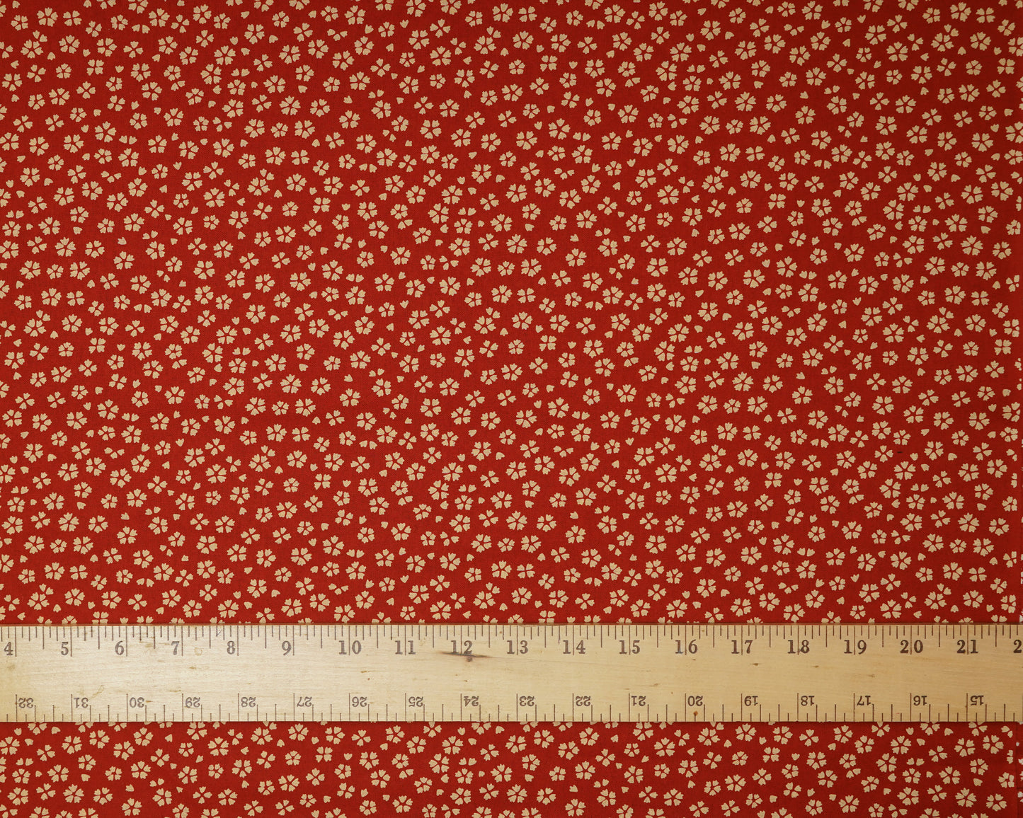Red fabric with small white floral pattern and a ruler at the bottom for scale.