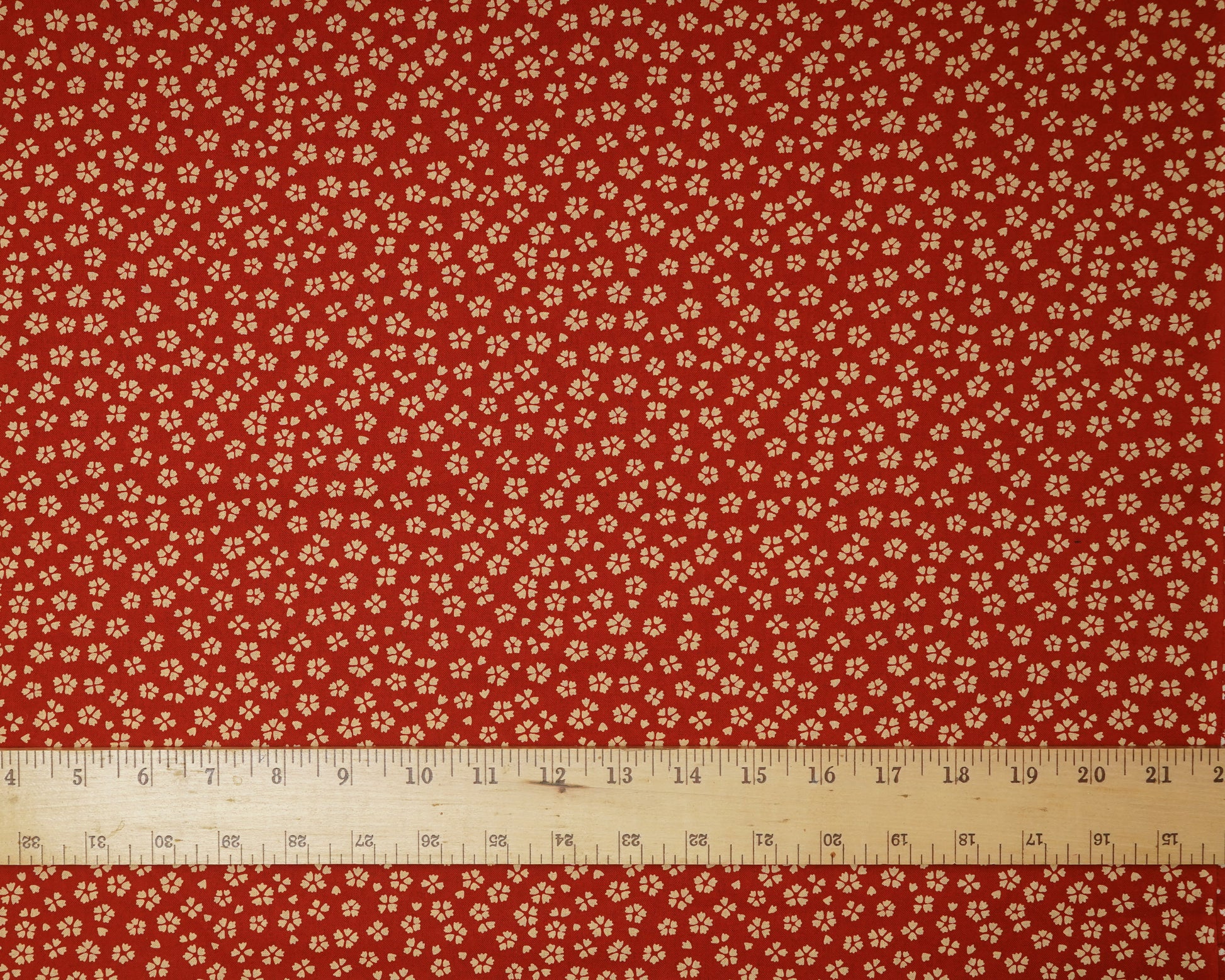 Red fabric with small white floral pattern and a ruler at the bottom for scale.