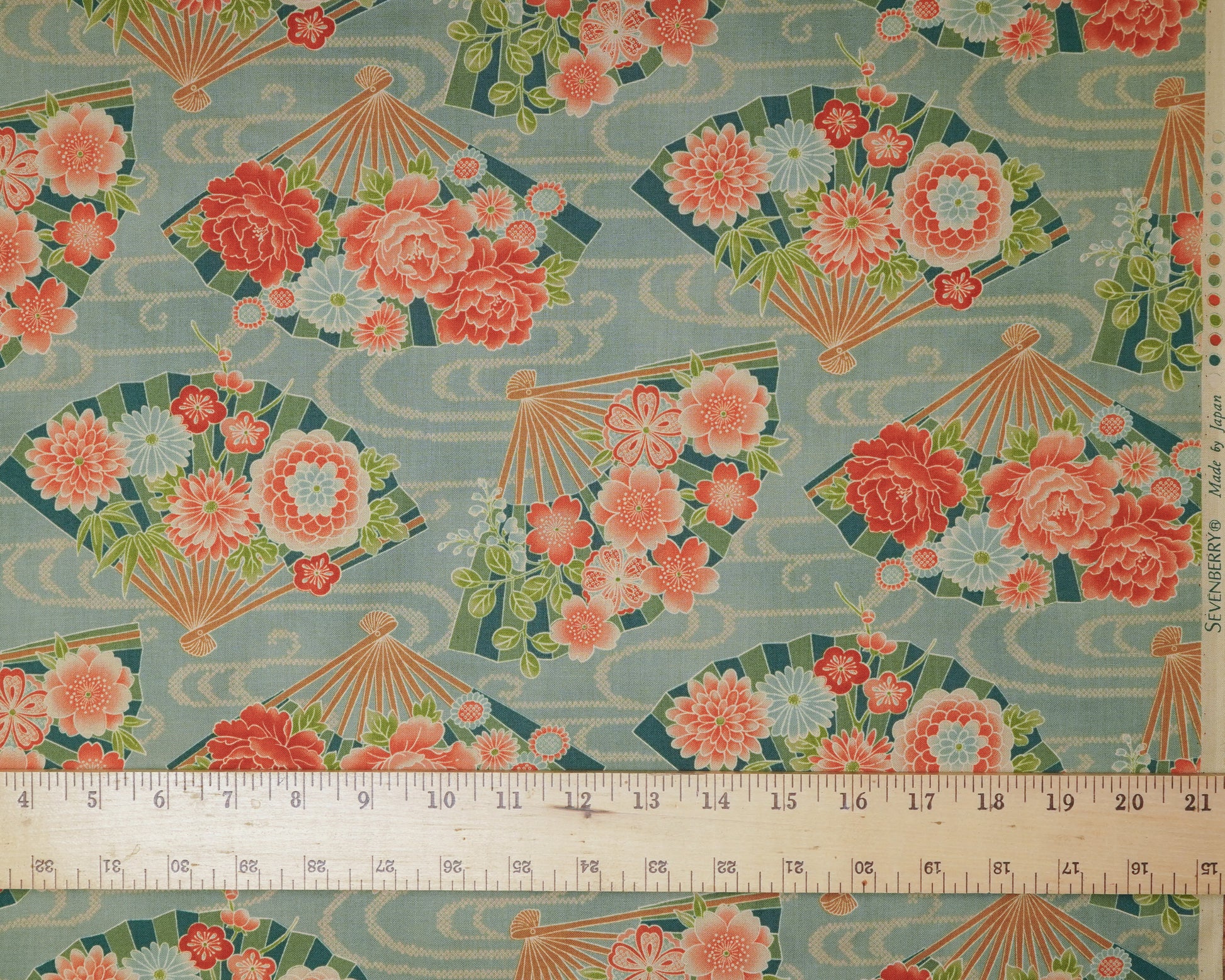 Fabric with floral and fan pattern on a blue background, ruler at the bottom for scale.