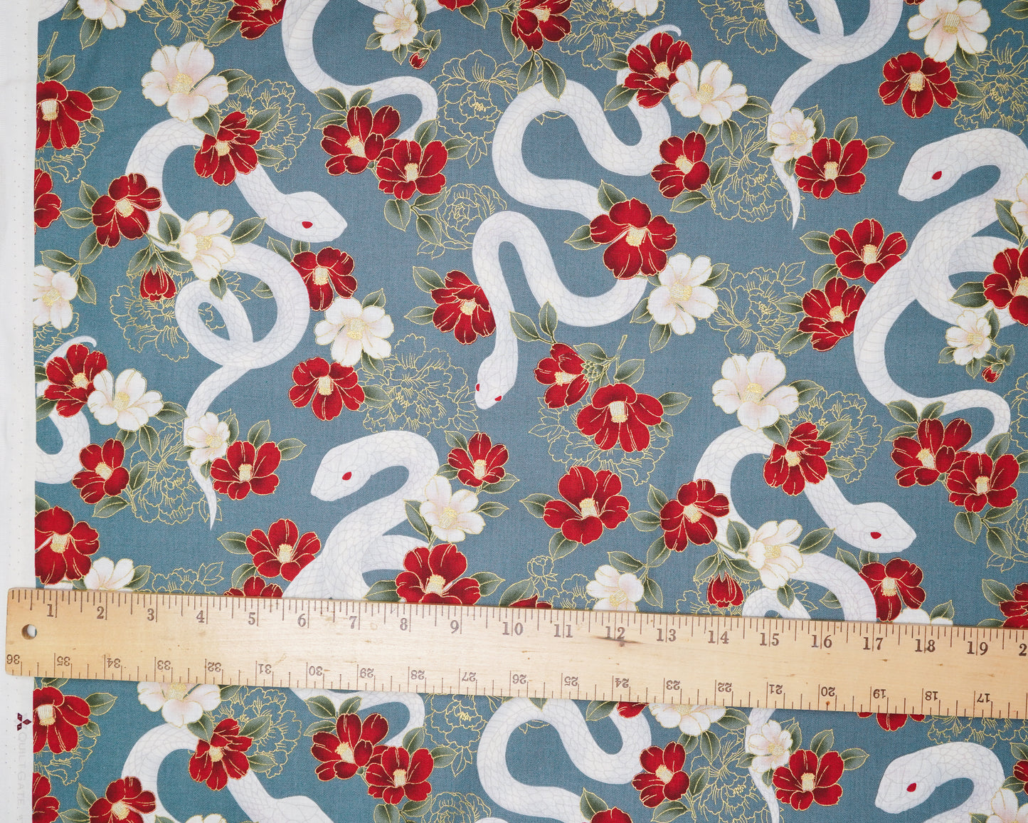 Fabric with white snakes and red flowers on a blue background, measured by a ruler.