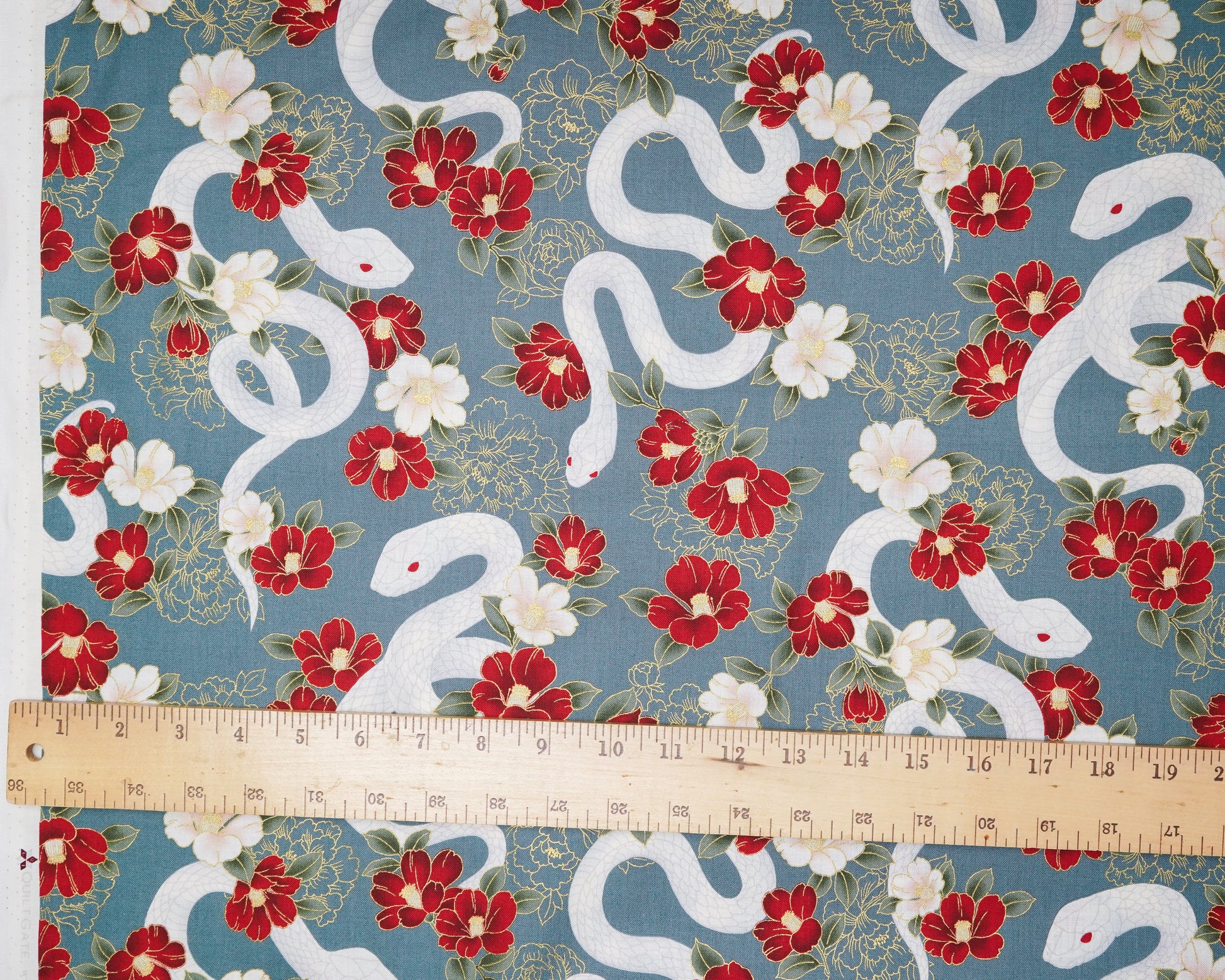 Fabric with white snakes and red flowers on a blue background, measured by a ruler.