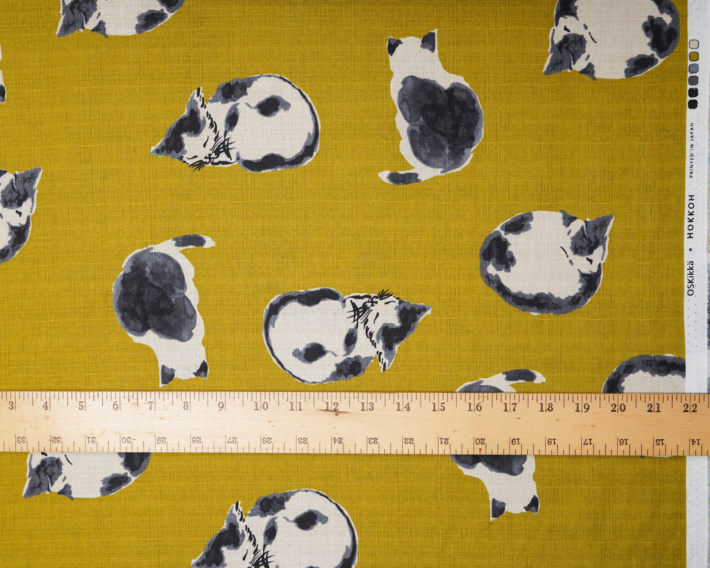 Fabric with black and white cat pattern on a mustard yellow background, ruler for scale.