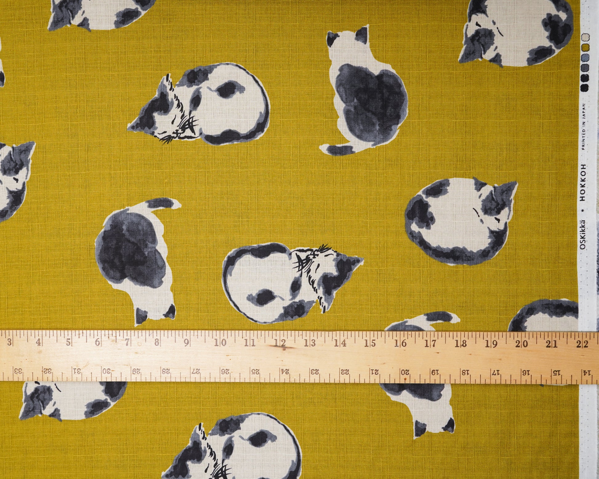 Fabric with black and white cat pattern on a mustard yellow background, ruler for scale.