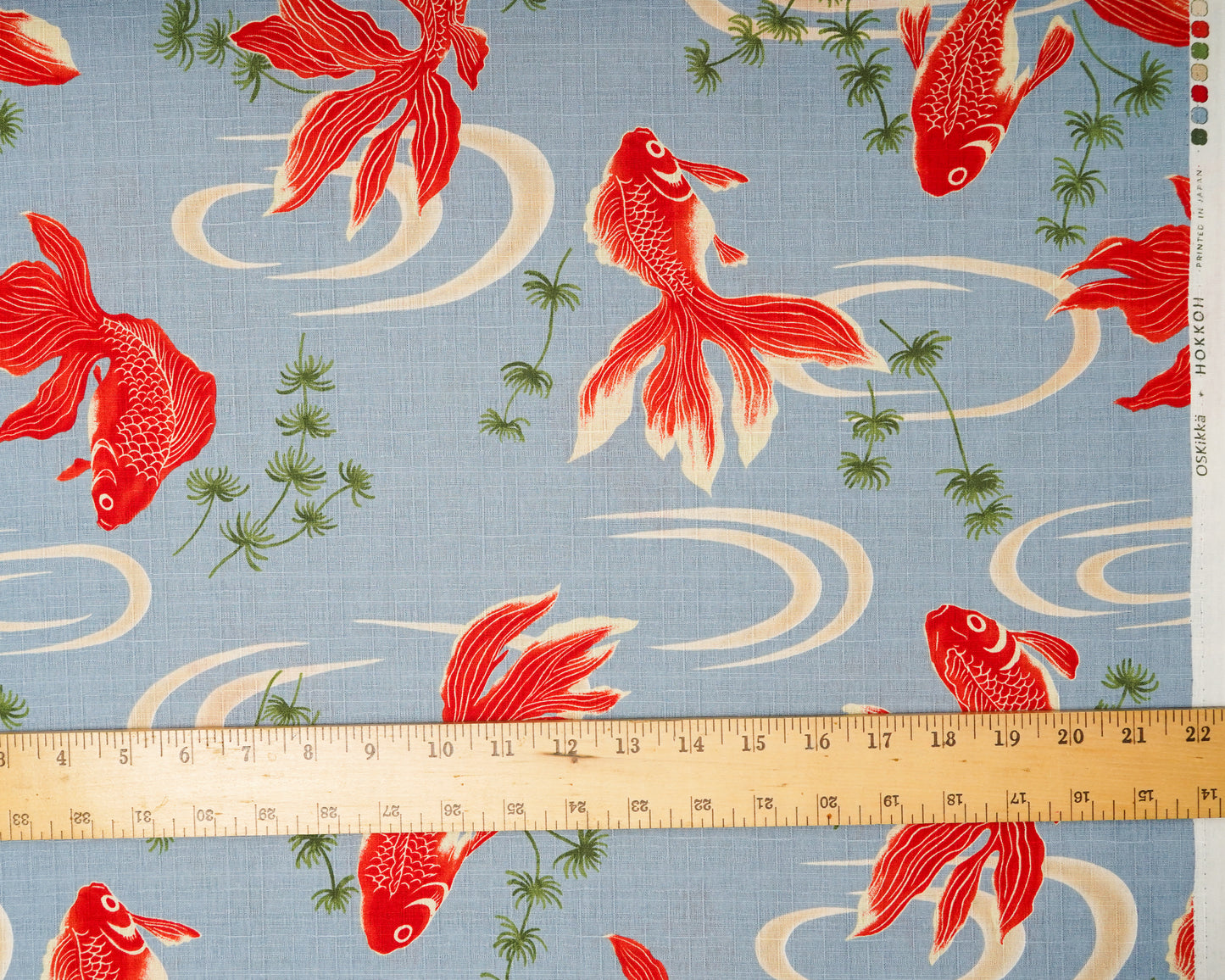 Fabric with red fish pattern on a blue background, ruler for scale