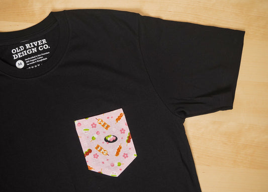 Black t-shirt with a pink pocket featuring cartoon sushi design on a wooden surface